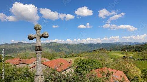 Croix de pierre au dessus d'un village. Paysage de campagne vallonnée l'été en Auvergne. Nature, collines, forêts, champs et prairies de Haute Loire en France.