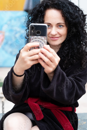 beautiful woman with dark curly hair in bathrobe photographing smiling with the smartphone