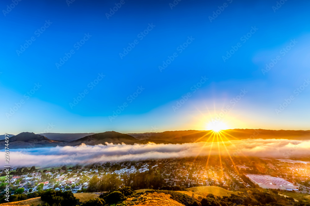 Fototapeta premium Sunburst above Clouds and Mountains, City