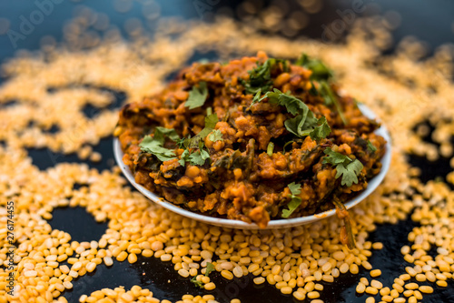 Famous Indian Punjabi dish i.e. Roasted dal with spinach in a glass plate on the wooden surface along with its main ingredients i.e. Unskinned split moong dal.