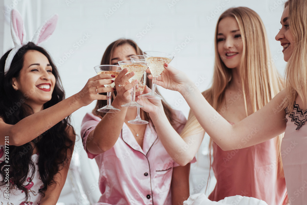 For the our happiness. Celebrating bachelorette in white bedroom. Girls smiles and drink champagne For the our happiness. Celebrating bachelorette in white bedroom. Girls smiles and drink champagne