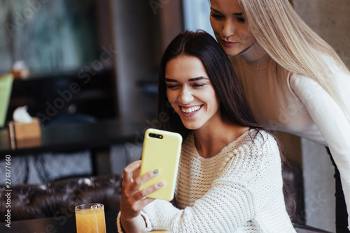Let's check our photo. In the restaurant. Two female friends sit indoors with yellow drink and use the smartphone