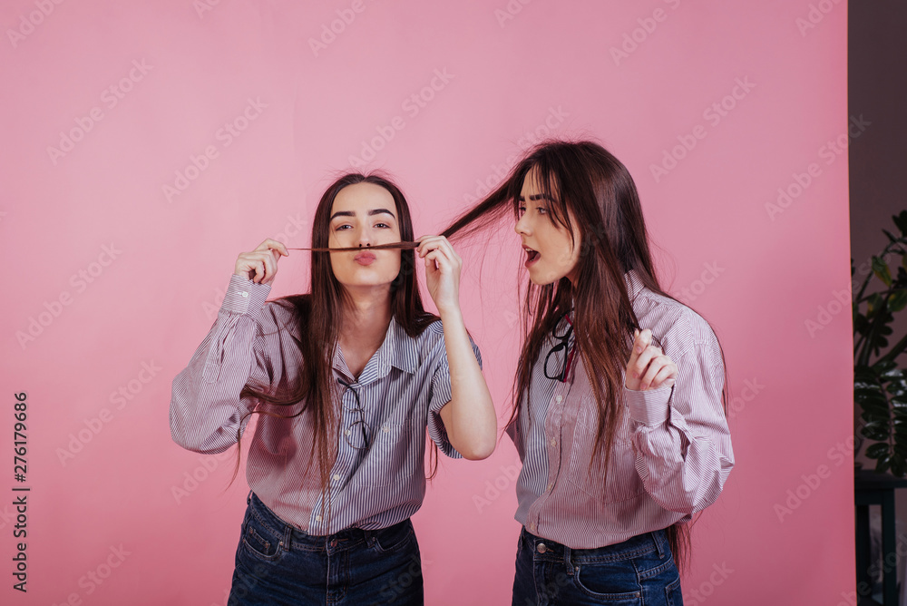 Imagine I was born a man with mustache that big. Two sisters twins standing and posing in the studio with white background Imagine I was born a man with mustache that big. Two sisters twins standing and posing in the studio with white background