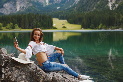 Young happy woman doing selfie on a rock by the lake