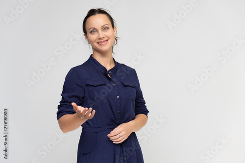 Portrait of a young pretty brunette woman of 30 years old in a simple plain blue dress with dark hair. Standing right in front of the camera, talking, showing hands, demonstrating emotions.