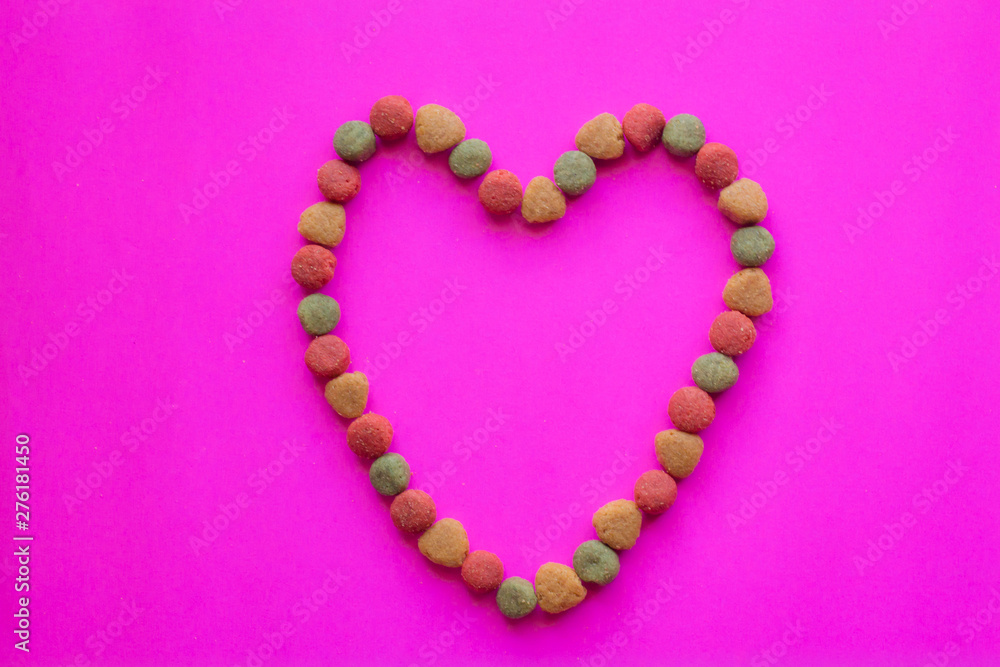 Creative valentines concept photo of Dog food and a heart be lovely on pink background.