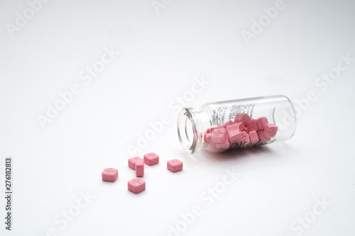 Glass vial with the pink pills on the white table.