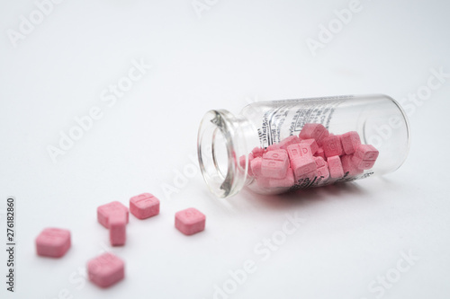 Glass vial with the pink pills on the white table.