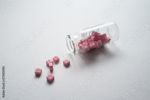 Glass vial with the pink pills on the white table.