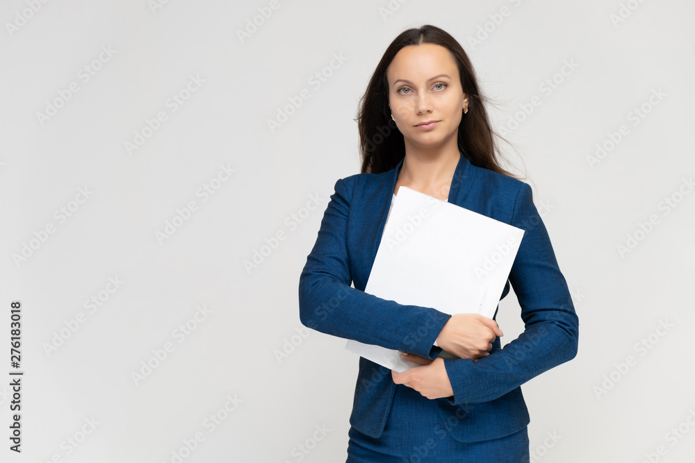 Portrait of a young pretty brunette manager woman of 30 years in a business blue suit with beautiful dark hair. Standing with a folder on a white background, talking, showing hands, with emotions Portrait of a young pretty brunette manager woman of 30 years in a business blue suit with beautiful dark hair. Standing with a folder on a white background, talking, showing hands, with emotions