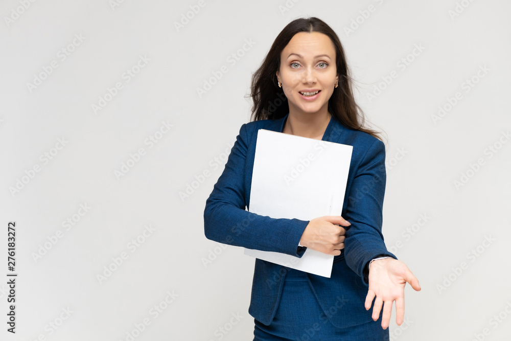 Portrait of a young pretty brunette manager woman of 30 years in a business blue suit with beautiful dark hair. Standing with a folder on a white background, talking, showing hands, with emotions Portrait of a young pretty brunette manager woman of 30 years in a business blue suit with beautiful dark hair. Standing with a folder on a white background, talking, showing hands, with emotions