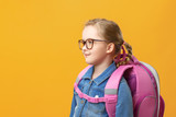 Little girl with a backpack in profile on a yellow background. Child with glasses close-up. Back to school. The concept of education.