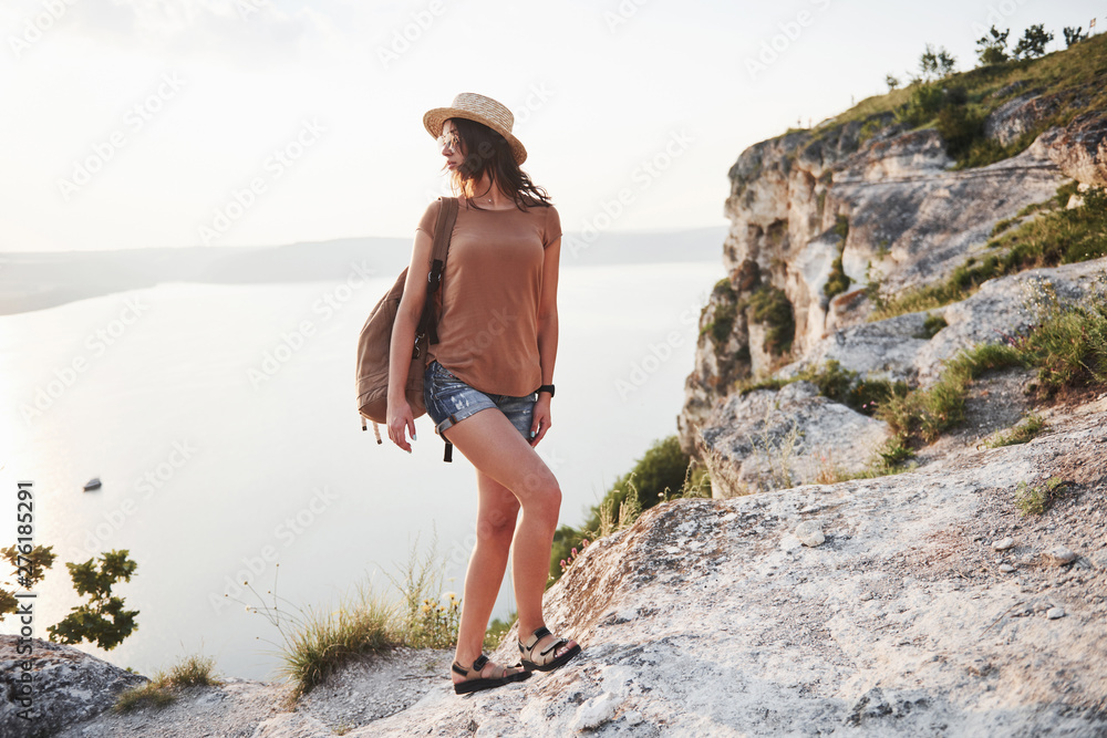 Naklejka premium Young girl with backpack enjoying sunset on peak of rocky mountain. Travel lifestyle adventure vacations concept