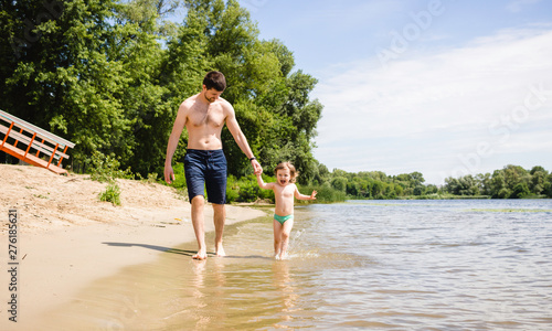 Happy excited toddler girl with her father running on water on a sandy beach. Kid with dad having fun