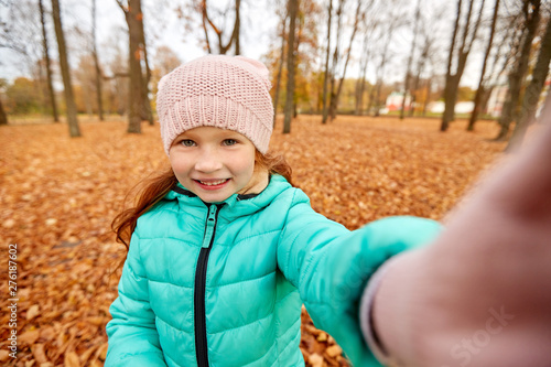 season and people concept - happy girl taking selfie at autumn park