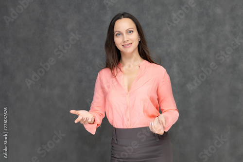 Portrait to the waist a young pretty brunette manager woman of 30 years in business clothes with beautiful dark hair. It is standing on a gray background, talking, showing hands, with emotions