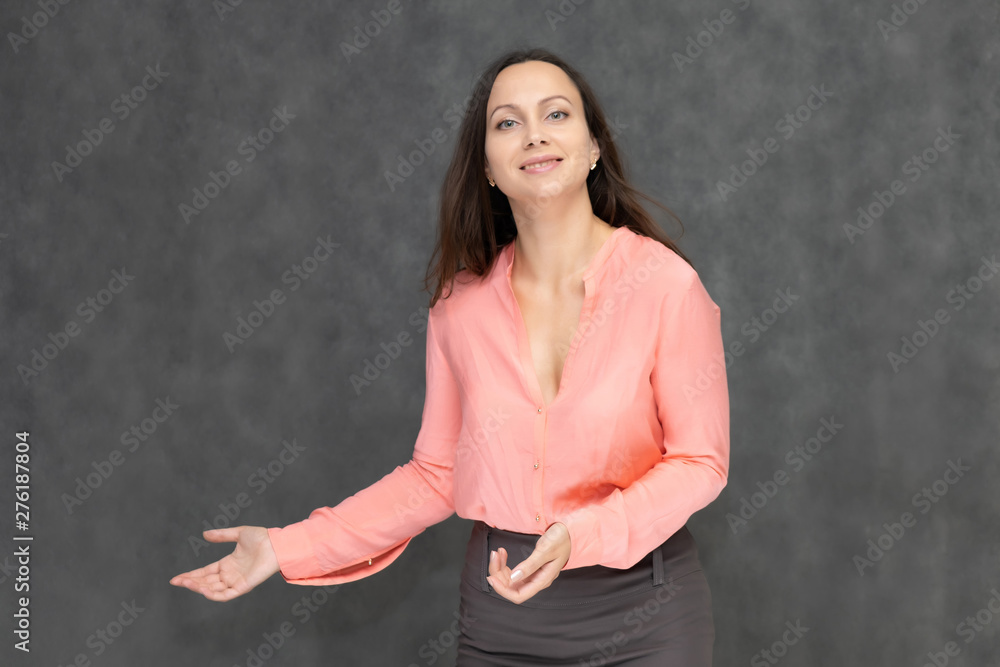 Portrait to the waist a young pretty brunette manager woman of 30 years in business clothes with beautiful dark hair. It is standing on a gray background, talking, showing hands, with emotions Portrait to the waist a young pretty brunette manager woman of 30 years in business clothes with beautiful dark hair. It is standing on a gray background, talking, showing hands, with emotions