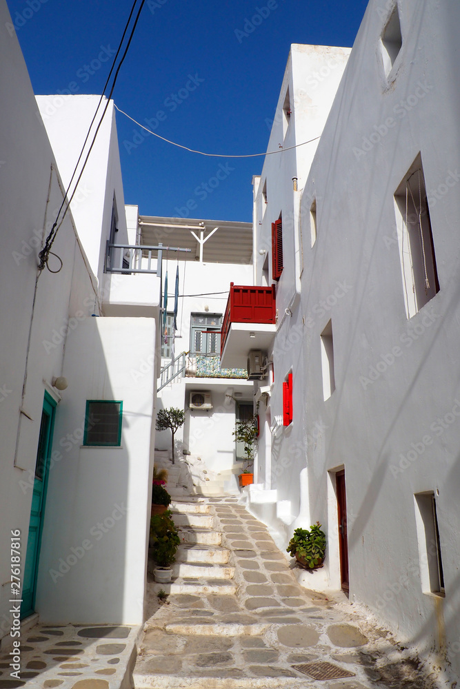 One of the charms of Mykonos, Greek island in the heart of the cyclades, are its narrow streets : white houses with small flowered balconies touching almost above paved streets