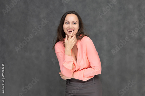 Portrait to the waist a young pretty brunette manager woman of 30 years in business clothes with beautiful dark hair. It is standing on a gray background, talking, showing hands, with emotions © Вячеслав Чичаев