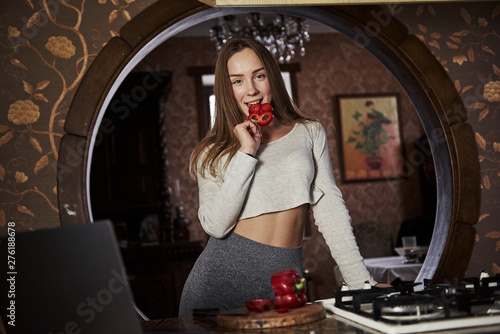 Taste fresh sliced red hot pepper. Pretty young woman standing in the modern kitchen near gas stove