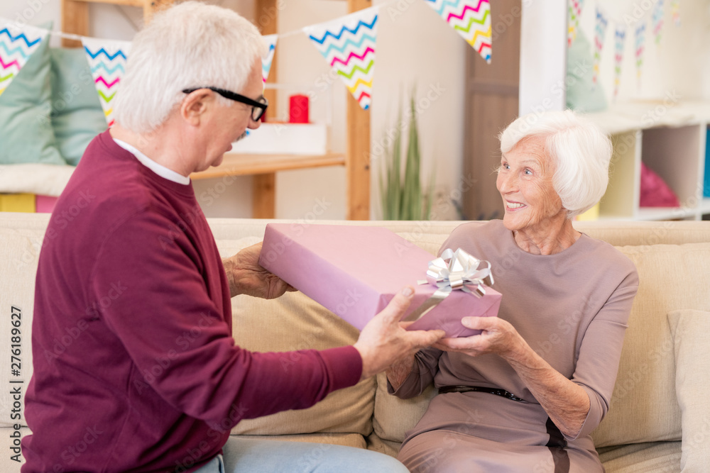 Obraz premium Cheerful senior female taking present from hands of her husband