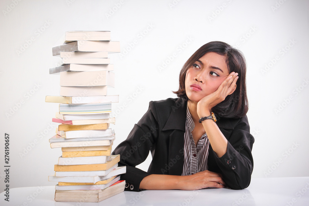 Stressed out young woman feels overwhelmed looking at stack of textbooks Stressed out young woman feels overwhelmed looking at stack of textbooks