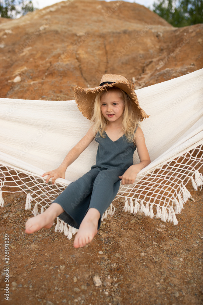 Little cute girl in stylish clothes on a background of rocks. Summer portrait of a little girl in a hat and cotton clothes for a magazine or advertisement