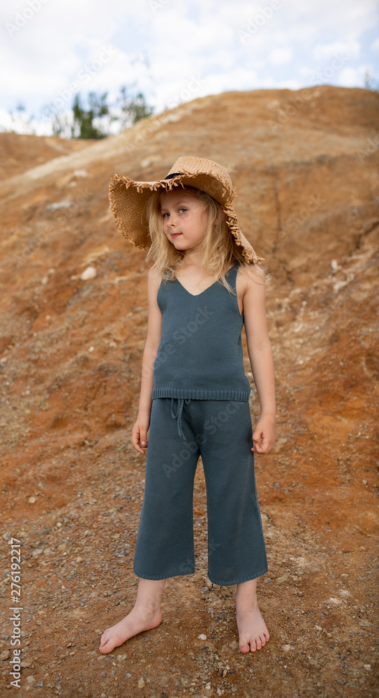 Little cute girl in stylish clothes on a background of rocks. Summer portrait of a little girl in a hat and cotton clothes for a magazine or advertisement Little cute girl in stylish clothes on a background of rocks. Summer portrait of a little girl in a hat and cotton clothes for a magazine or advertisement