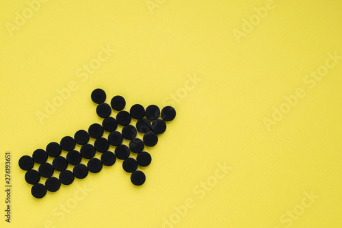 Medical activated carbon in the form of an arrow on a yellow background. Top view, copy space.