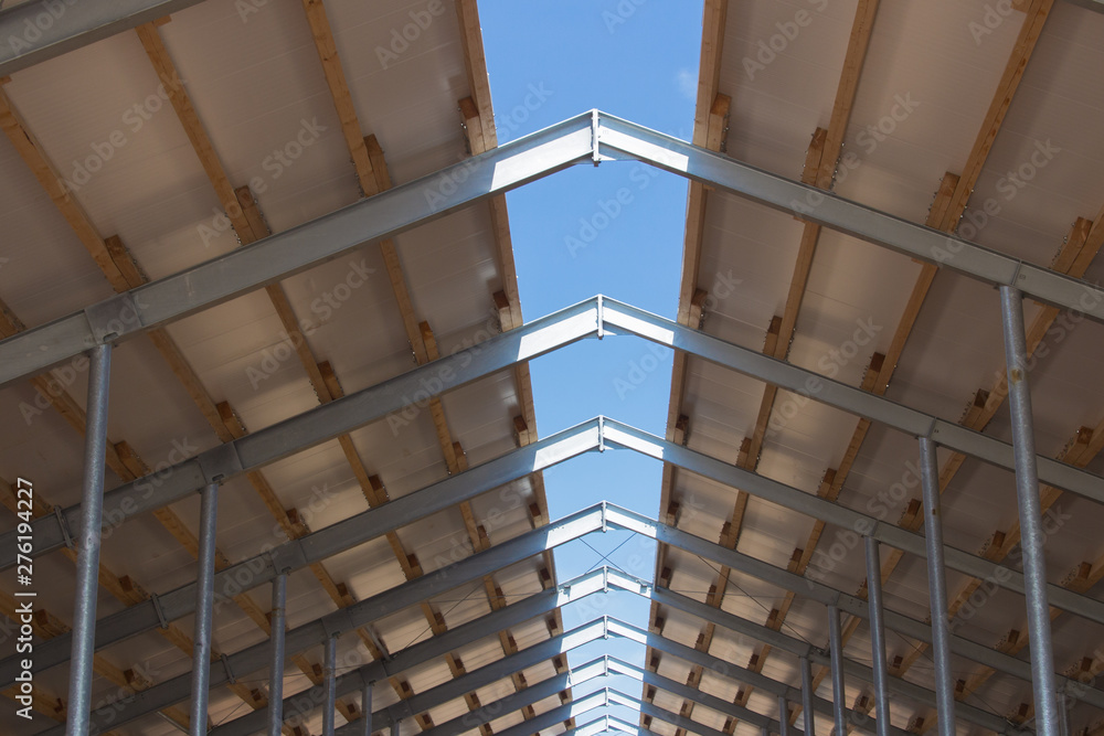 Roof structure consisting of a metal frame, wooden beams and foam insulation against a blue sky. Agricultural constructions. The roof of the new barn.