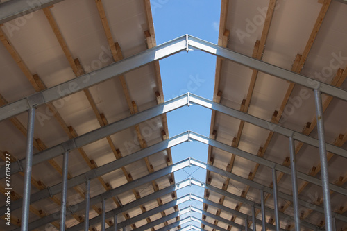 Roof structure consisting of a metal frame, wooden beams and foam insulation against a blue sky. Agricultural constructions. The roof of the new barn. © Vasiliy Ulyanov