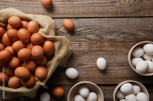 top view of chicken eggs in bowls on wooden table with cloth