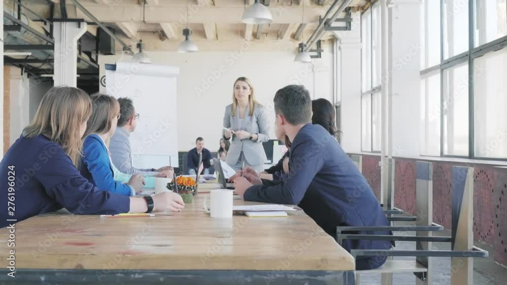The team leader discusses with colleagues and conducts a presentation using a flipchart, describes business processes. Employees sit at the table. Office life. Coworking. Modern interior in loft style The team leader discusses with colleagues and conducts a presentation using a flipchart, describes business processes. Employees sit at the table. Office life. Coworking. Modern interior in loft style