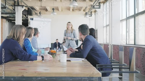 The team leader discusses with colleagues and conducts a presentation using a flipchart, describes business processes. Employees sit at the table. Office life. Coworking. Modern interior in loft style