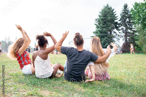 Group of friends sitting on grass and having fun at summer music festival