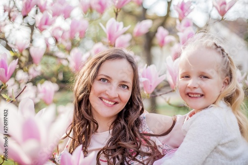 Beautiful young mother and little daughter near a blooming magnolia. Spring. Pink blooms.