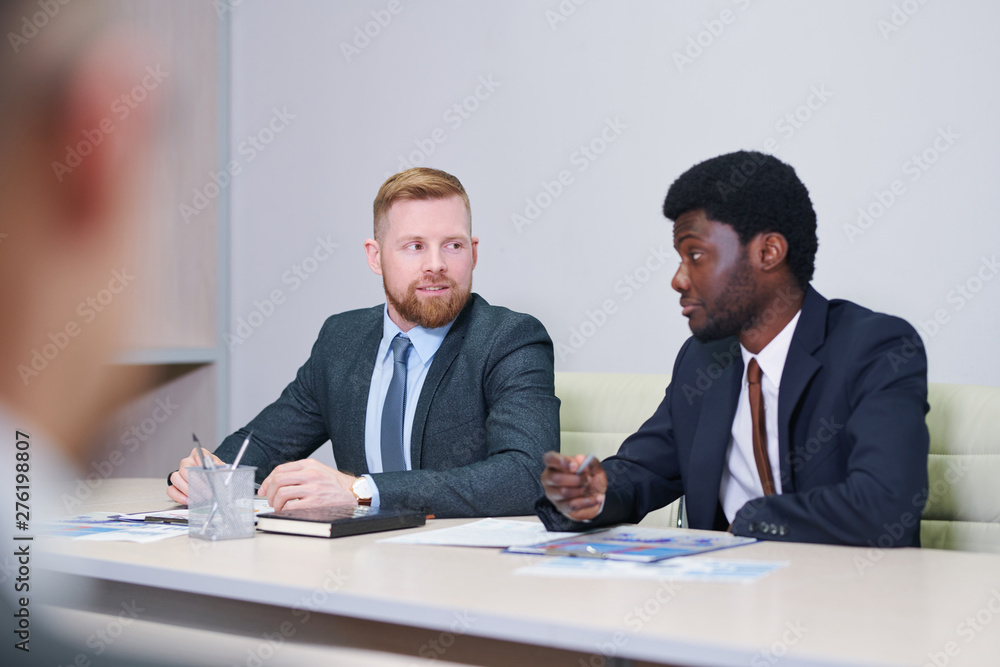 Two young intercultural businessmen discussing working points Two young intercultural businessmen discussing working points