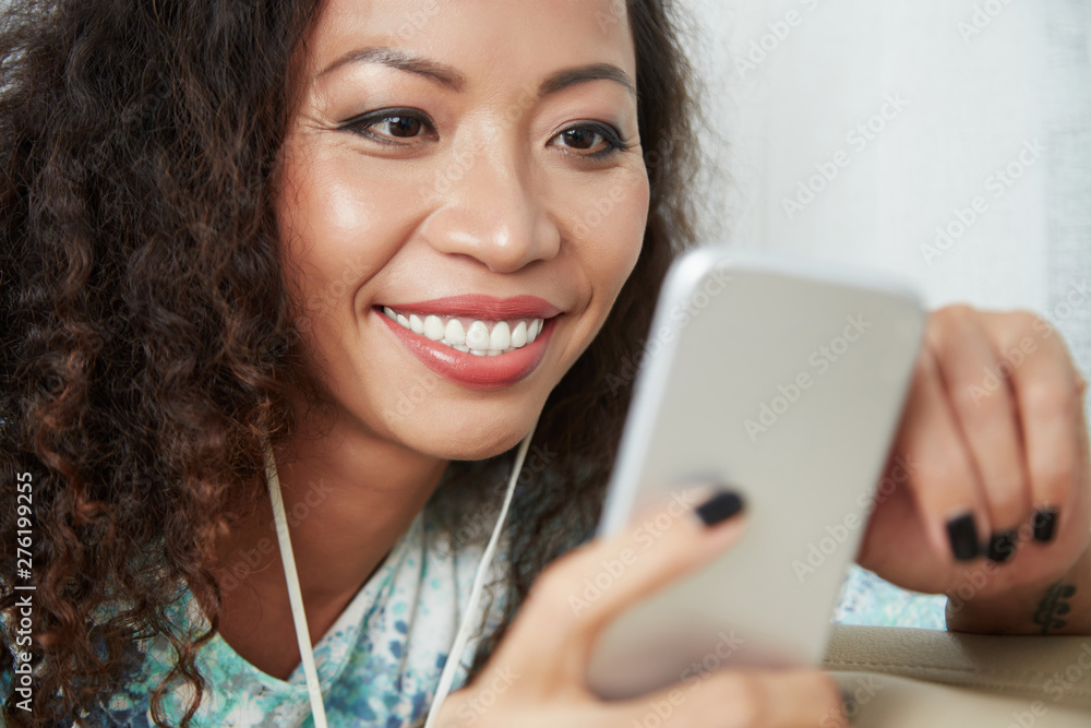 Face of happy pretty Vietnamese woman smiling when reading text messages from her friends on smartphone Face of happy pretty Vietnamese woman smiling when reading text messages from her friends on smartphone