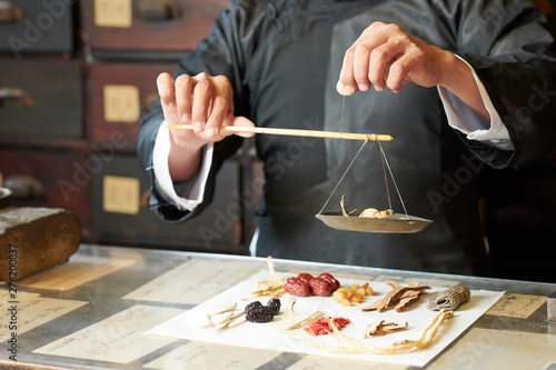 Close-up image of traditional Chinese medicine practitioner using special scales to weight dry plant roots for treatment