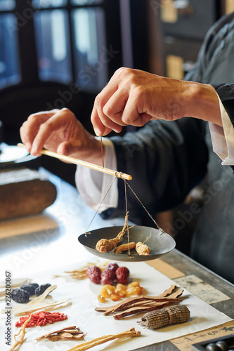 Obraz na plátně Hands of tradiotional Asian medicine practitioner weighting herbs and roots on o