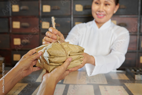 Obraz na plátně Chinese apothecary worker giving package of dried medicine ingredients to patien