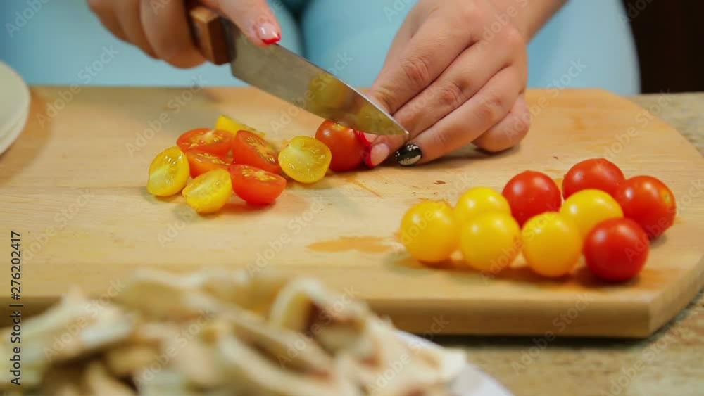 A woman is cutting a yellow and red cherry tomato with a knife on a wooden board. time laps. A woman is cutting a yellow and red cherry tomato with a knife on a wooden board. time laps.
