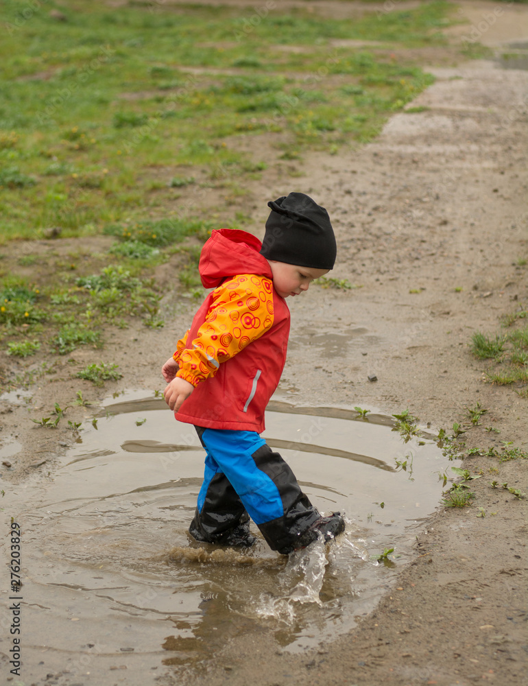The dwr of the shellpants and leather boots with nanocoating protect the kid from mud and water. Kid playing in the puddle wearing outdoor wheather resistant clothing and footwear.