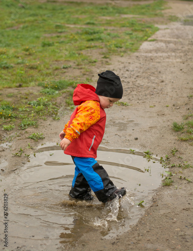 Obraz na płótnie The dwr of the shellpants and leather boots with nanocoating protect the kid from mud and water. Kid playing in the puddle wearing outdoor wheather resistant clothing and footwear. w salonie