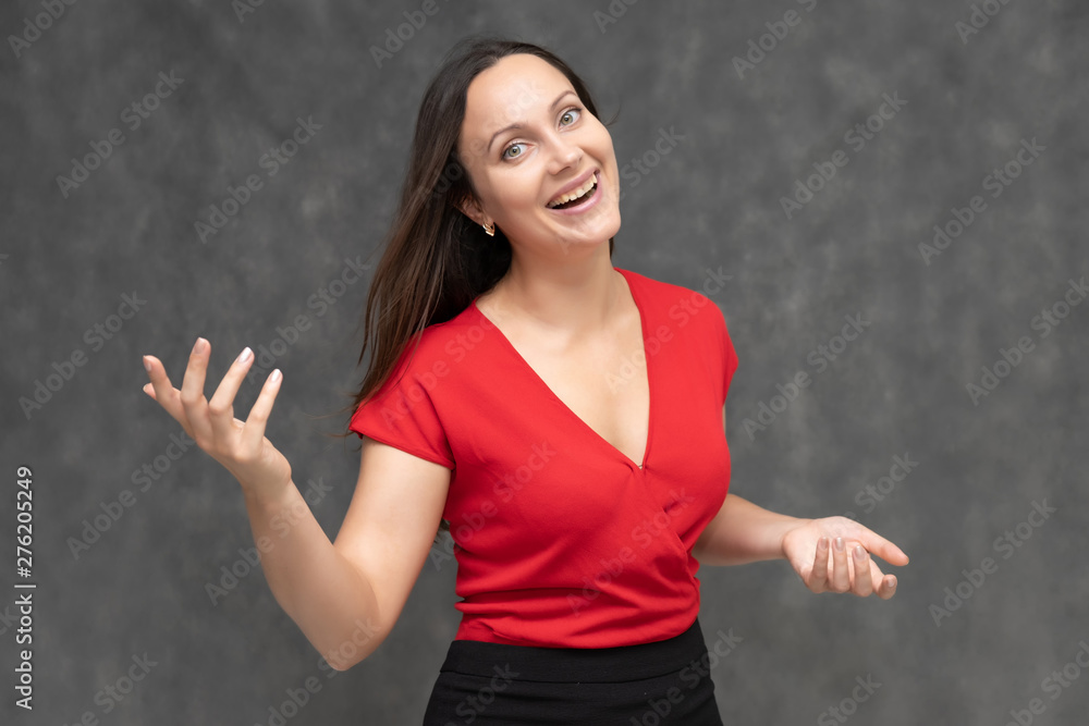 Portrait to the waist of a young pretty brunette woman of 30 years old in a bright red sweater with beautiful dark hair. It is standing on a gray background, talking, showing hands, with emotions Portrait to the waist of a young pretty brunette woman of 30 years old in a bright red sweater with beautiful dark hair. It is standing on a gray background, talking, showing hands, with emotions