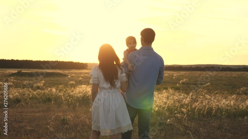 Family playing with their daughter in sunshine. happy child sitting on the hands of parents. Mom and dad play with their little daughter in the park at sunset. family walk with the baby in park.