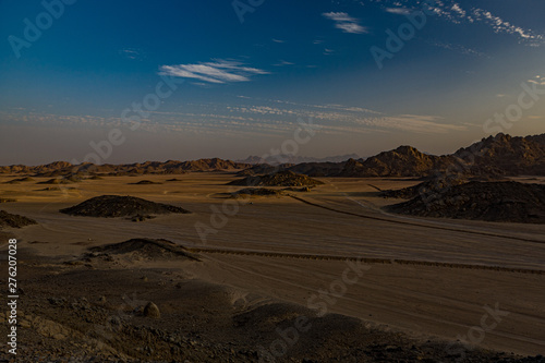 Safari and travel to Africa - extreme adventures or science expedition in a stone desert. Sahara desert at sunrise - mountain landscape with dust on skyline  hills and traces of the off-road car
