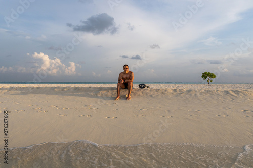 Handsome sexy topless male model relaxed sitting on the beach