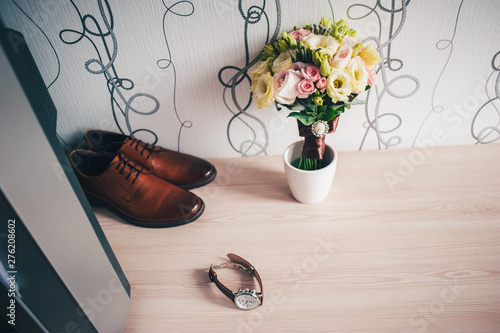 stylish wedding brown men shoes lying on a light table. White background. Accessories groom. bridal bouquet of roses, leather watch, wedding morning.