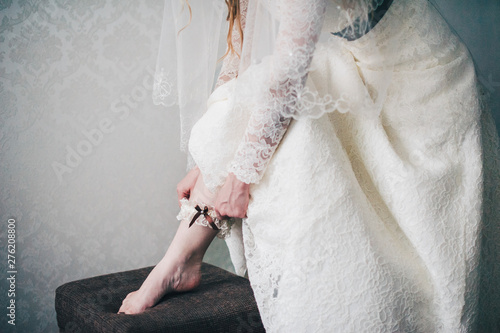 hand puts on a wedding garter armband on his leg. close-up. Morning Bride. wedding day. Stylish dress. mignonette. close up. part dresses. Against the background of white wall apartment.